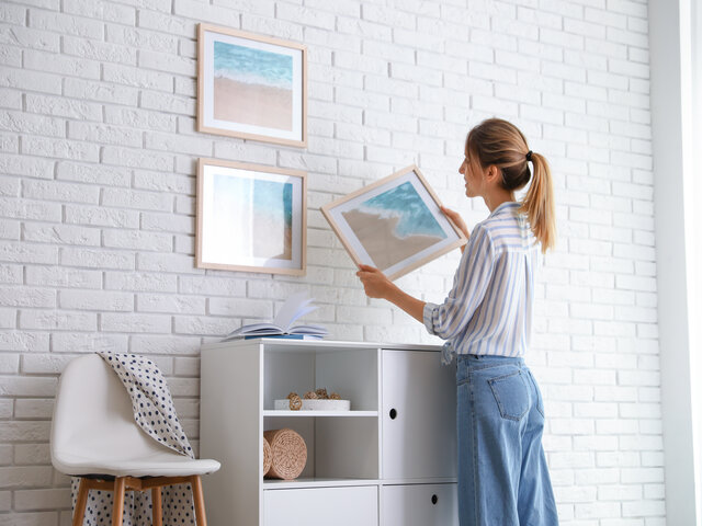 a female interior stylist hanging picture on white brick wall